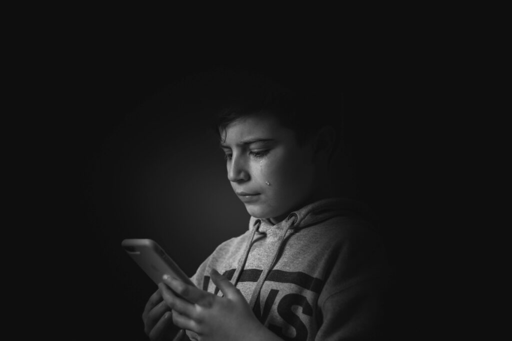 A monochromatic portrait of a boy holding a smartphone, expressing sadness.