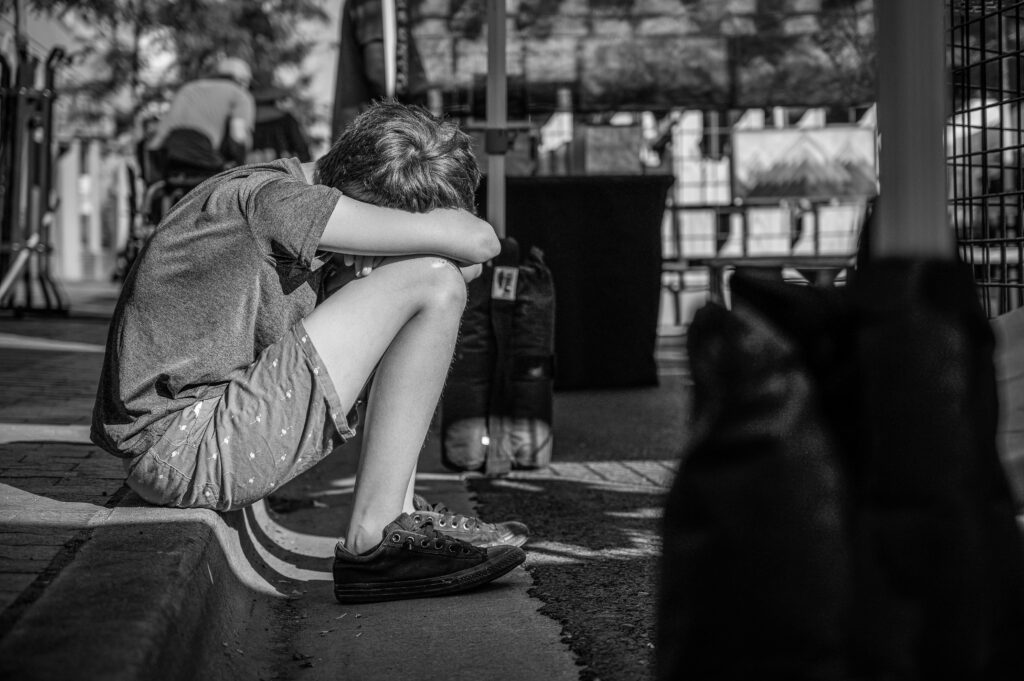 A child sitting alone on a curb, depicting solitude and contemplation in a monochrome city setting.