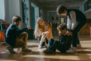 How to Help a Child with Anxiety: A Psychologist’s Guide Four kids engaged in a playful or bullying encounter inside a school.
