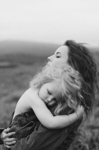 A touching black and white photo of a mother embracing her child outdoors, capturing affection and warmth.